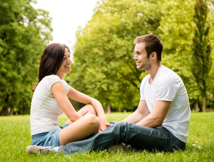 Young happy couple talking together outdoor - sitting on grass