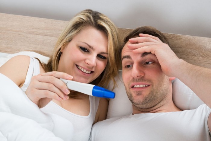 Couple Looking At A Positive Pregnancy Test In Bedroom