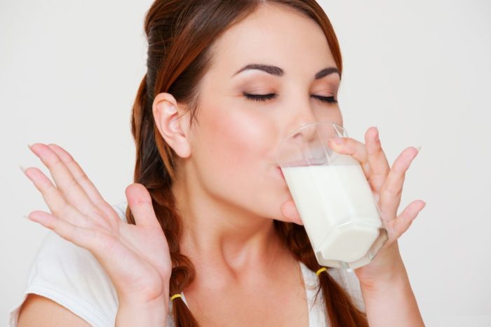 happy young woman drinking milk over grey background